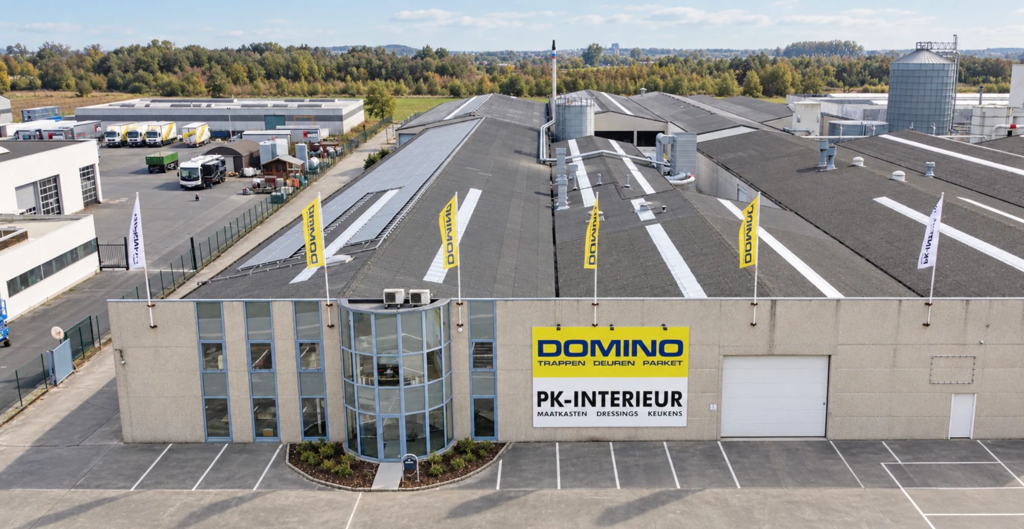 Luchtfoto van het Domino-bedrijfsgebouw met vlaggen en de productiehallen in Kruisem