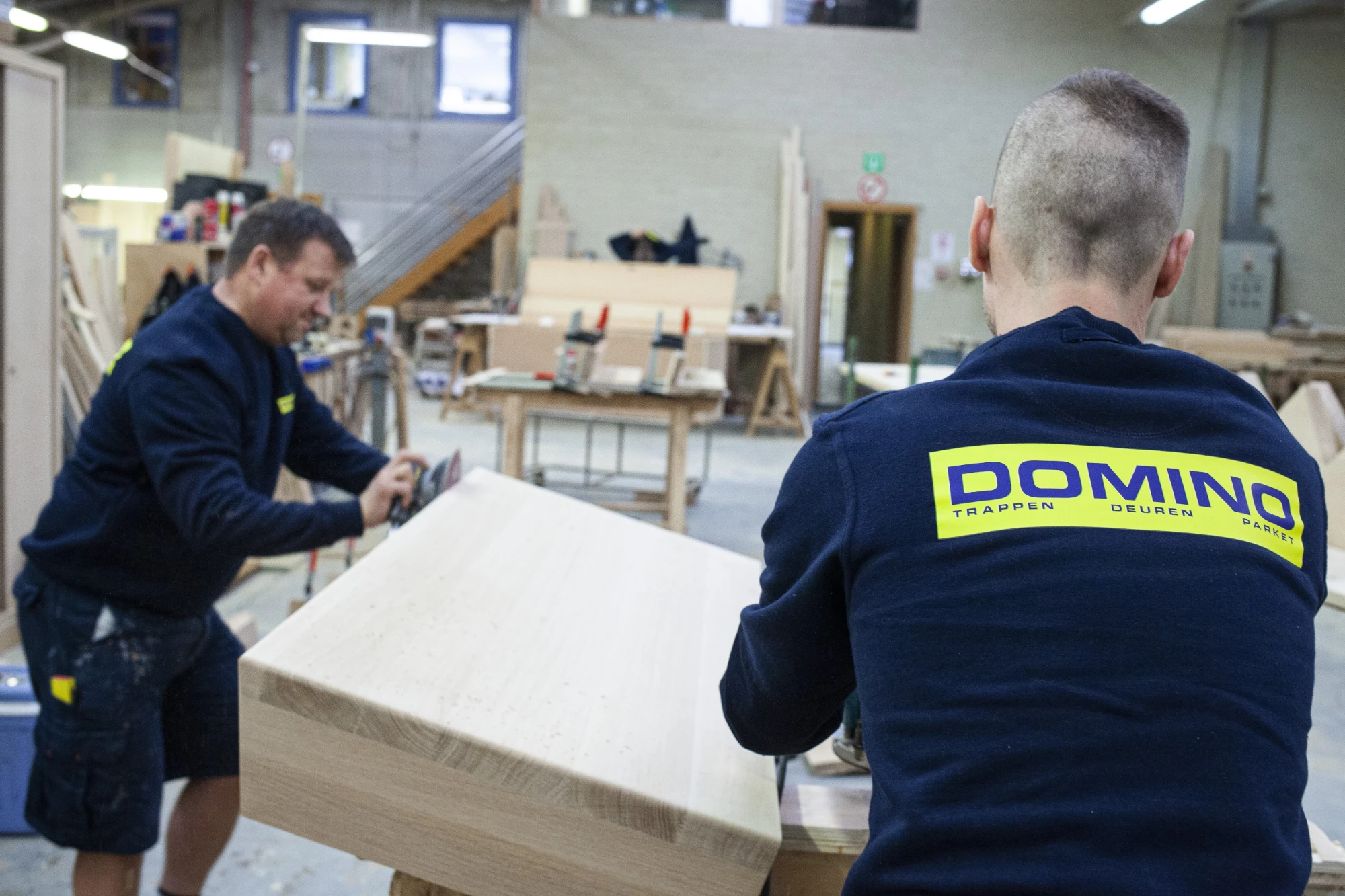 Twee medewerkers van Domino schuren een trede in het atelier